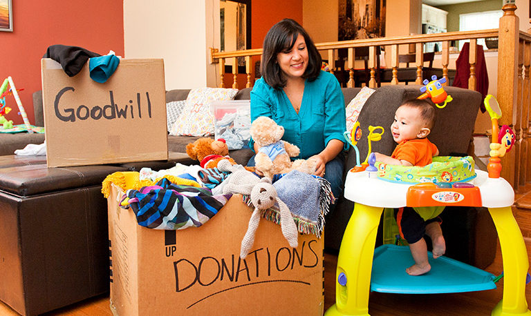 a mother packs cardboard boxes with household goods while her baby smiles nearby