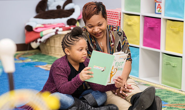 a woman helps a young girl read a children's book in a classroom