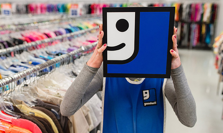 a Goodwill employee holds the Goodwill logo on front of their face for a fun photo