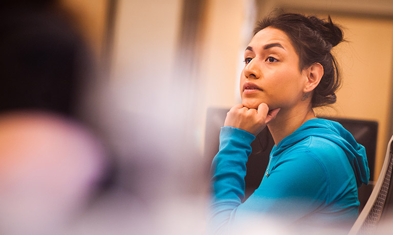 a woman in a blue sweatshirt looks toward front of classroom