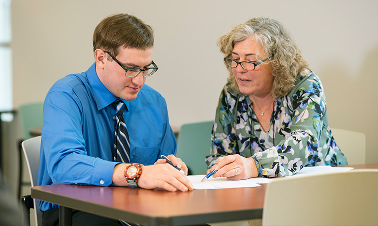 a middle-aged woman helps a young man review his work resume