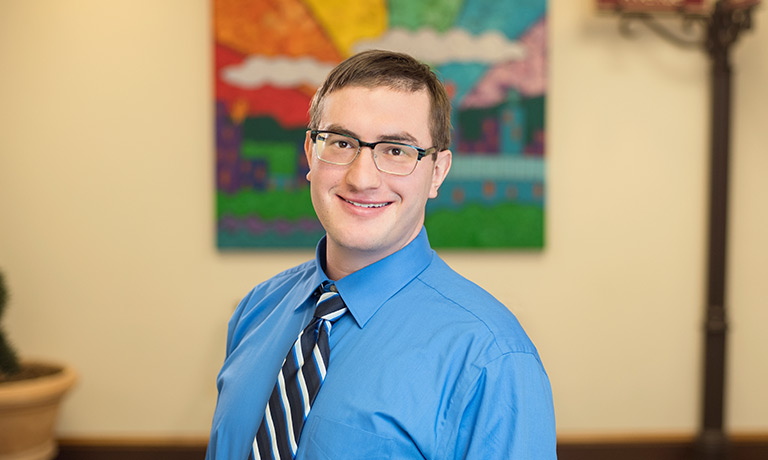 a young man wearing a blue shirt and striped tie smiles for the camera in a classroom