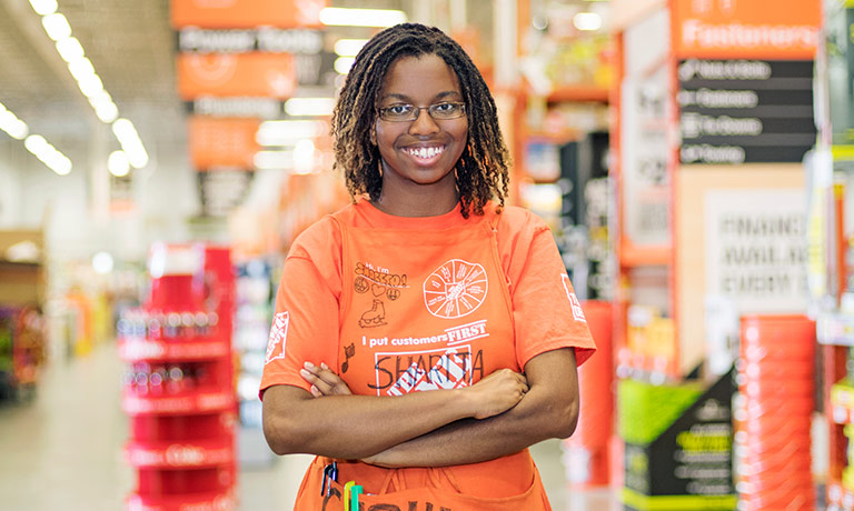 a young female employee of a home improvement store wears an orange apron and smiles for the camera