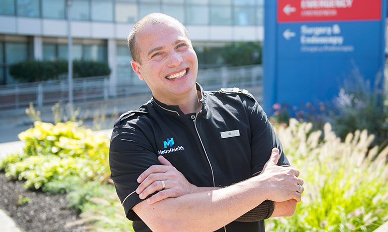 a man smiles for the camera in front of the hospital where he works