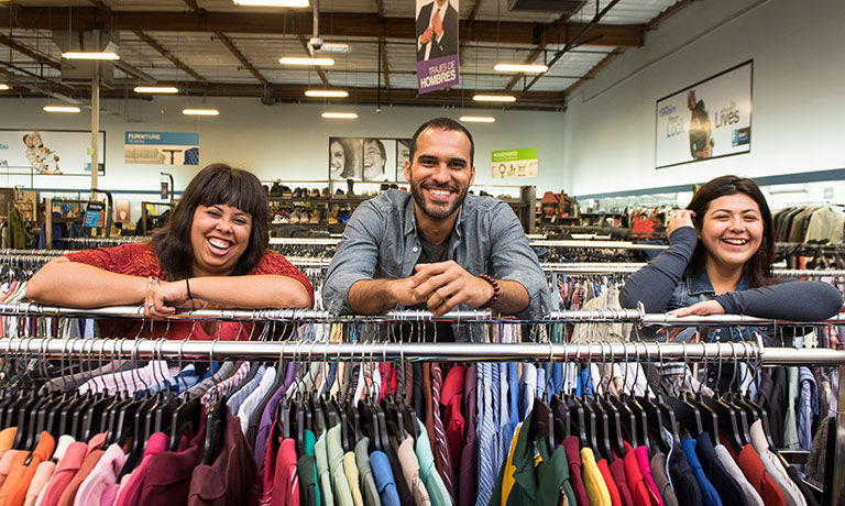 three Goodwill customers smile while leaning on a clothing rack in the store